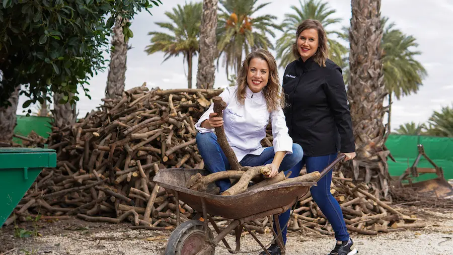 Noelia y Lidia con una carretilla de sarmientos junto a las palmeras